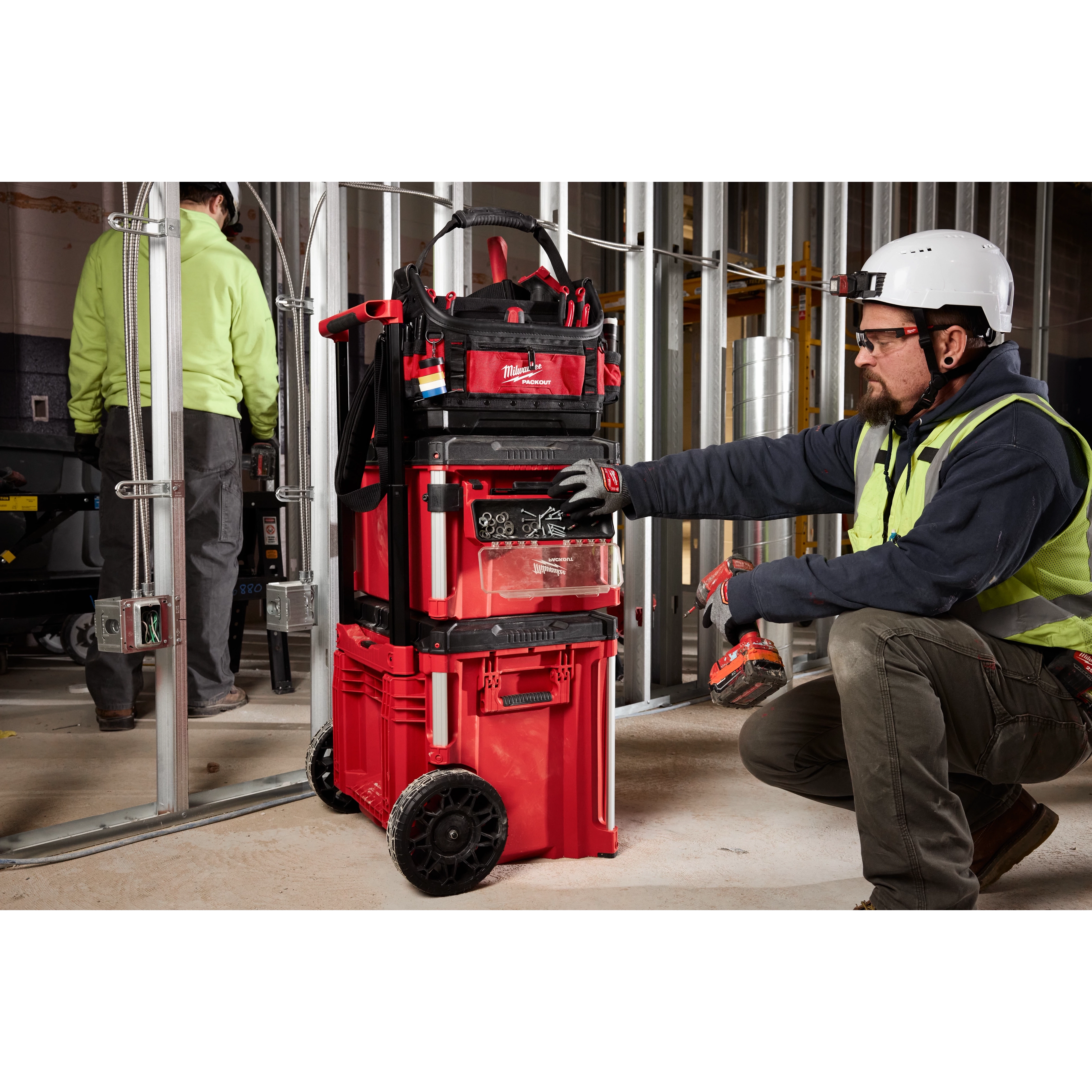 The PACKOUT Tool Box Magnetic Bin Attachment is shown being used on a construction site, attached to a red rolling tool box system.