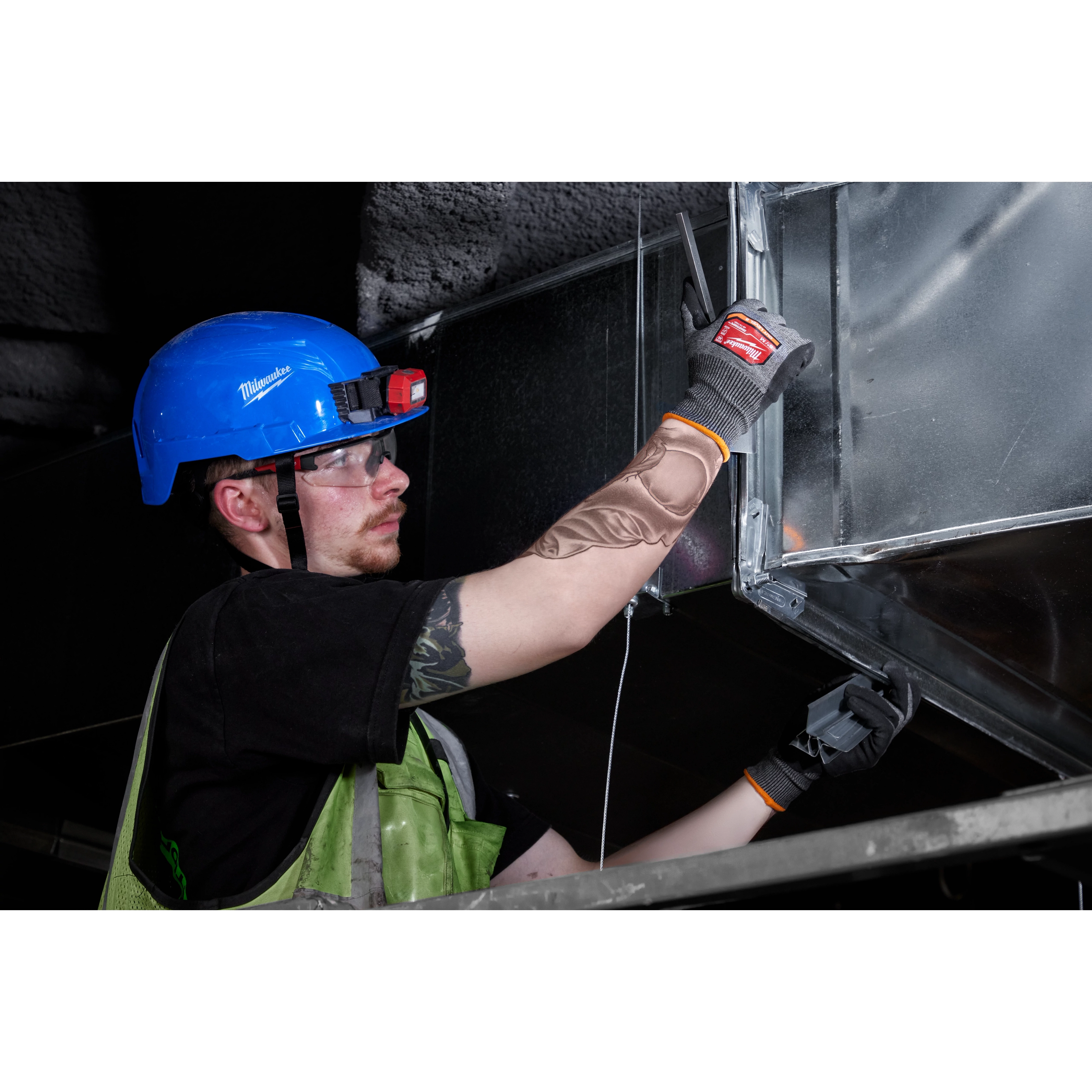 A worker in safety gear installs metal ductwork wearing Cut Level 8 High-Dexterity Nitrile Dipped Gloves - L, with a blue helmet.