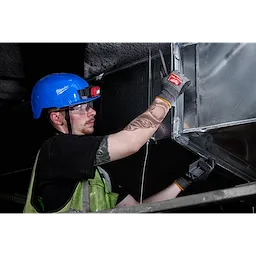 A worker in safety gear installs metal ductwork wearing Cut Level 8 High-Dexterity Nitrile Dipped Gloves - L, with a blue helmet.
