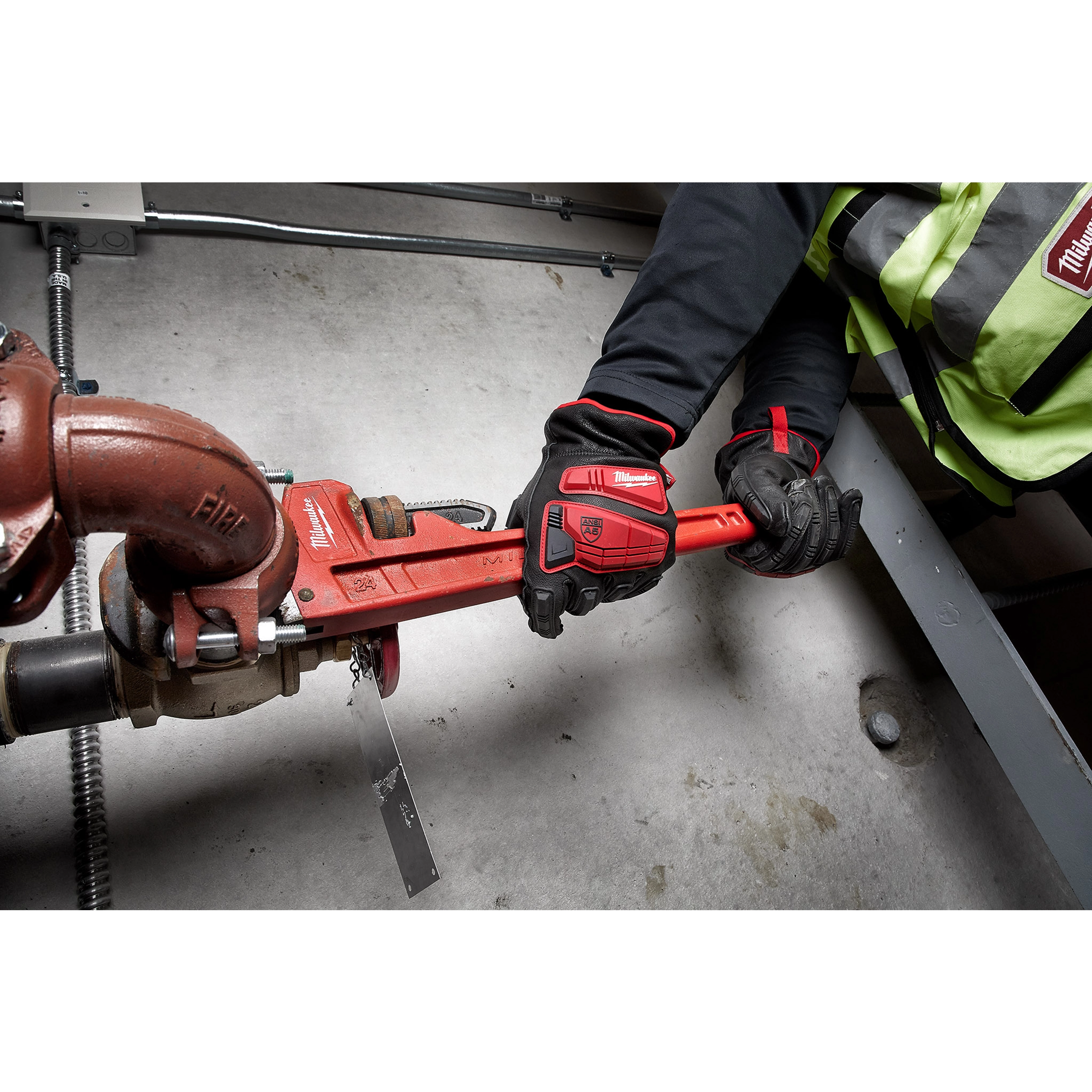 Person wearing Impact Cut Level 5 Goatskin Leather Gloves is tightening a red pipe wrench onto a valve in an industrial setting.
