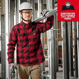 A person wearing a red and black GRIDIRON flannel shirt with a hard hat and gloves works at a construction site.