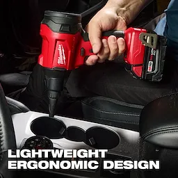 A person uses the M18™ Brushless Precision Blower to clean a car's cupholder area. The tool is red and black with "Milwaukee" branding, featuring a lightweight ergonomic design.