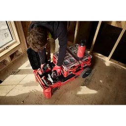 Worker organizing tools in a PACKOUT Compact Rolling Tool Chest inside a partially framed room.