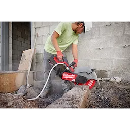 A worker is using a Milwaukee saw fitted with a 14" DIAMOND ULTRA™ Segmented Turbo, General Purpose Diamond Blade to cut through concrete at a construction site. They are wearing a green shirt, gloves, and a hard hat. The concrete wall and gravel ground are visible around the work area.