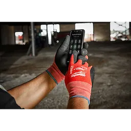 A person wearing Cut Level 2 Nitrile Dipped Gloves - L operates a smartphone in a construction area with a partially visible background.