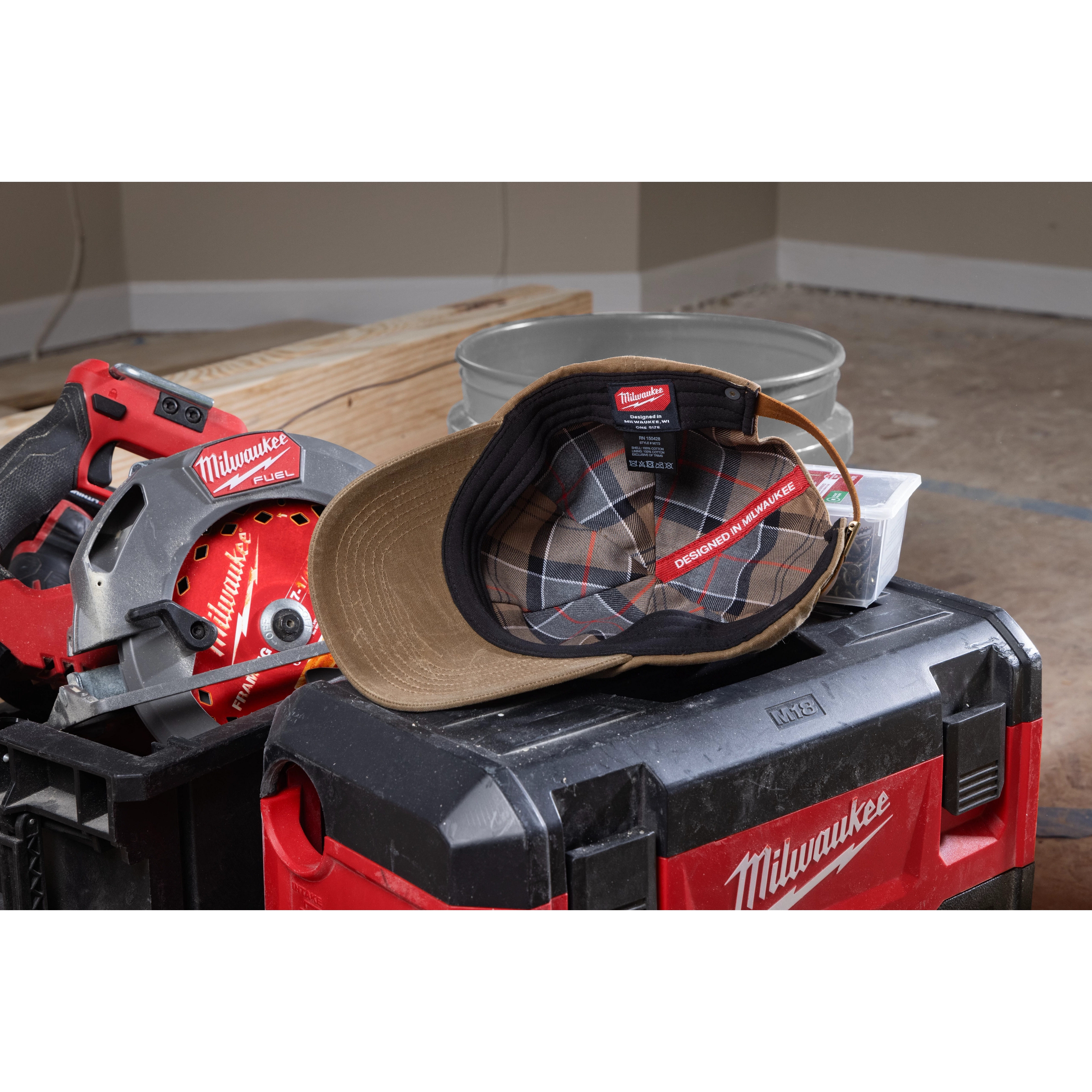 Waxed Canvas Adjustable Hat with a plaid inner lining displayed open on a toolbox, surrounded by power tools and construction materials.