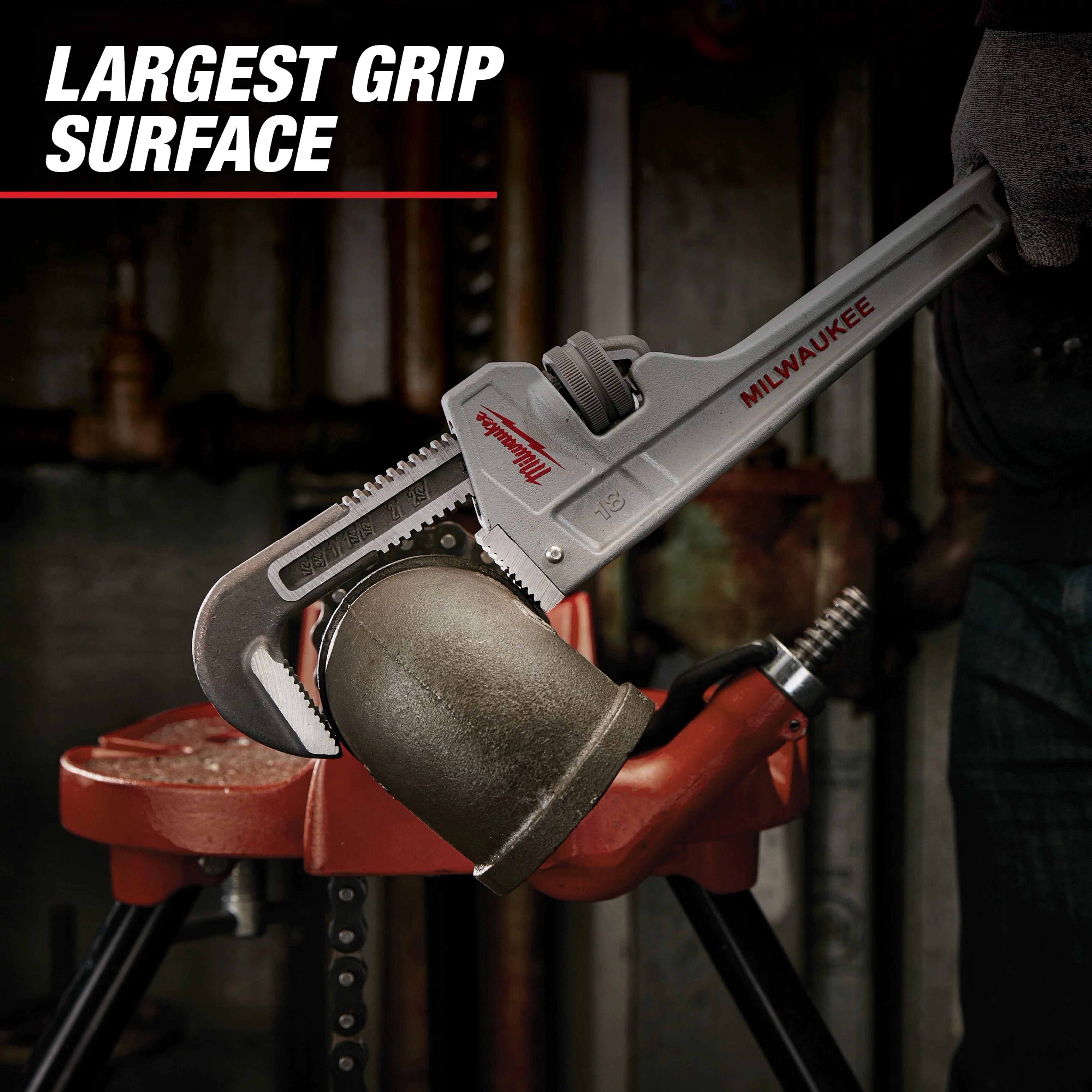 The Milwaukee adjustable pipe wrench is being used to grip a large metal pipe in a workshop. The text "LARGEST GRIP SURFACE" is displayed in the upper left corner.