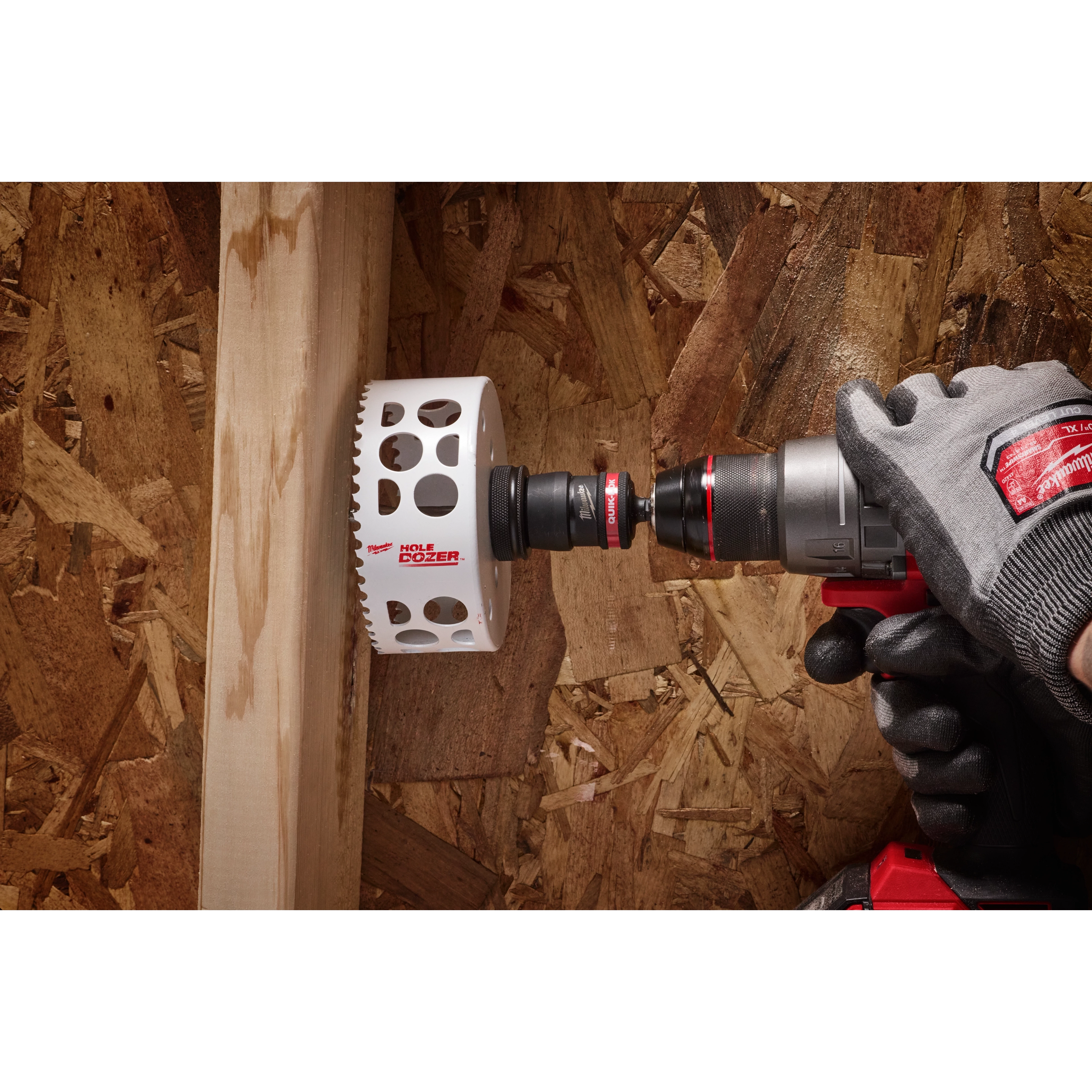 A gloved hand using a power drill with a 3/8" QUIK-LOK™ Arbor Set is shown drilling a hole in a piece of wood attached to an OSB board.