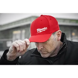 Person wearing a red Milwaukee Fitted Hat, with the Milwaukee logo prominently displayed, and a black jacket outdoors.