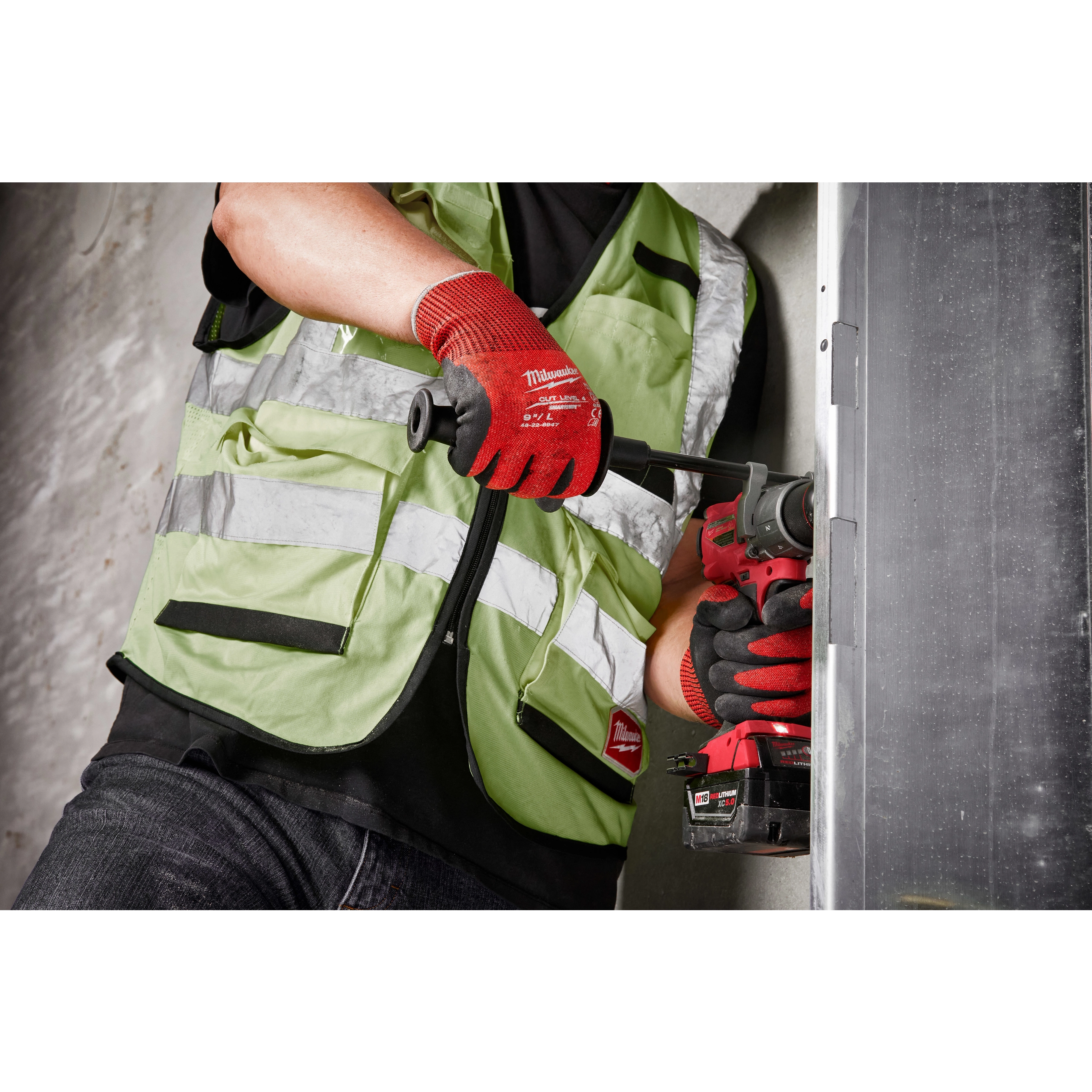 Person using a power tool wears red Cut Level 4 Nitrile Dipped Glove - L, with high-visibility green safety vest, working on a metal surface.