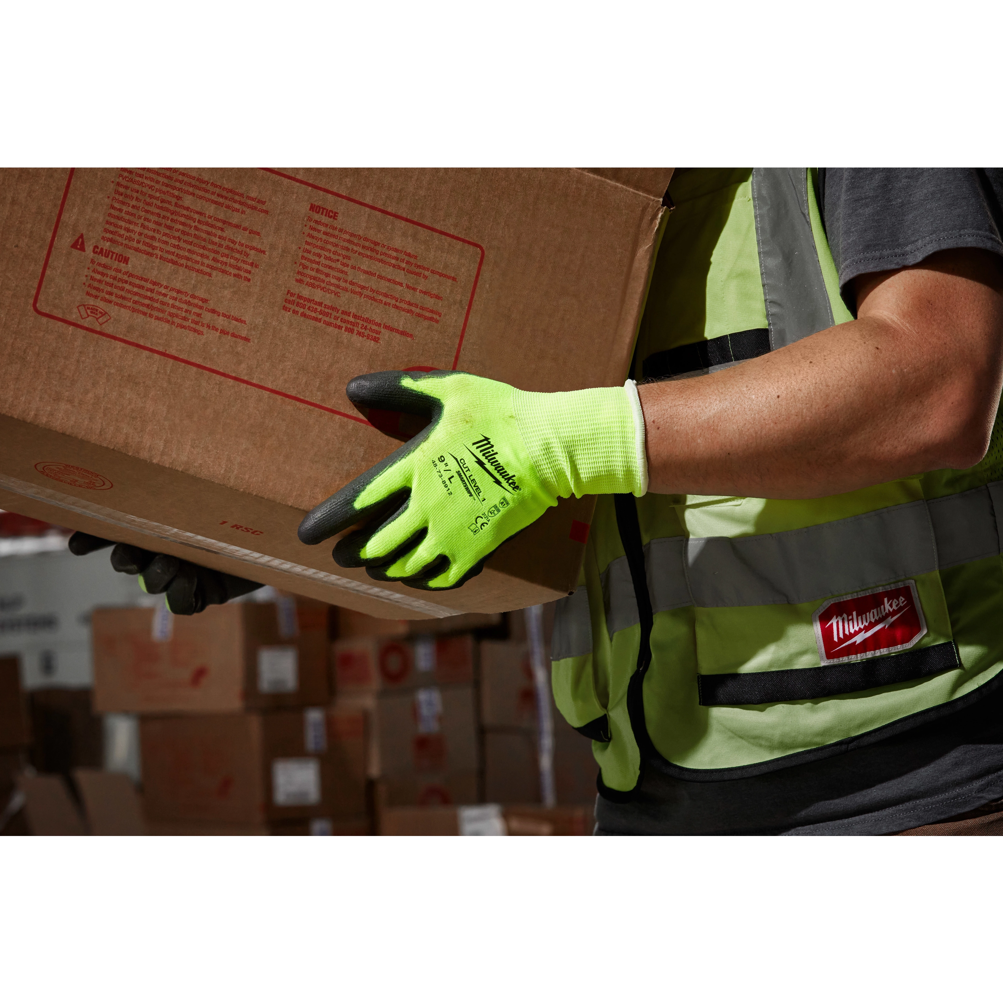 Person wearing a High Visibility Cut Level 1 Polyurethane Dipped Glove - L while handling a cardboard box in a warehouse.