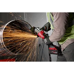 A person uses the M18 FUEL™ 4 1/2" - 6" Dual Trigger Braking Grinder, Paddle Switch w/ ONE KEY™ to cut through a metal pipe, producing bright sparks. The grinder is red with black accents and is held with both hands while wearing protective gloves.