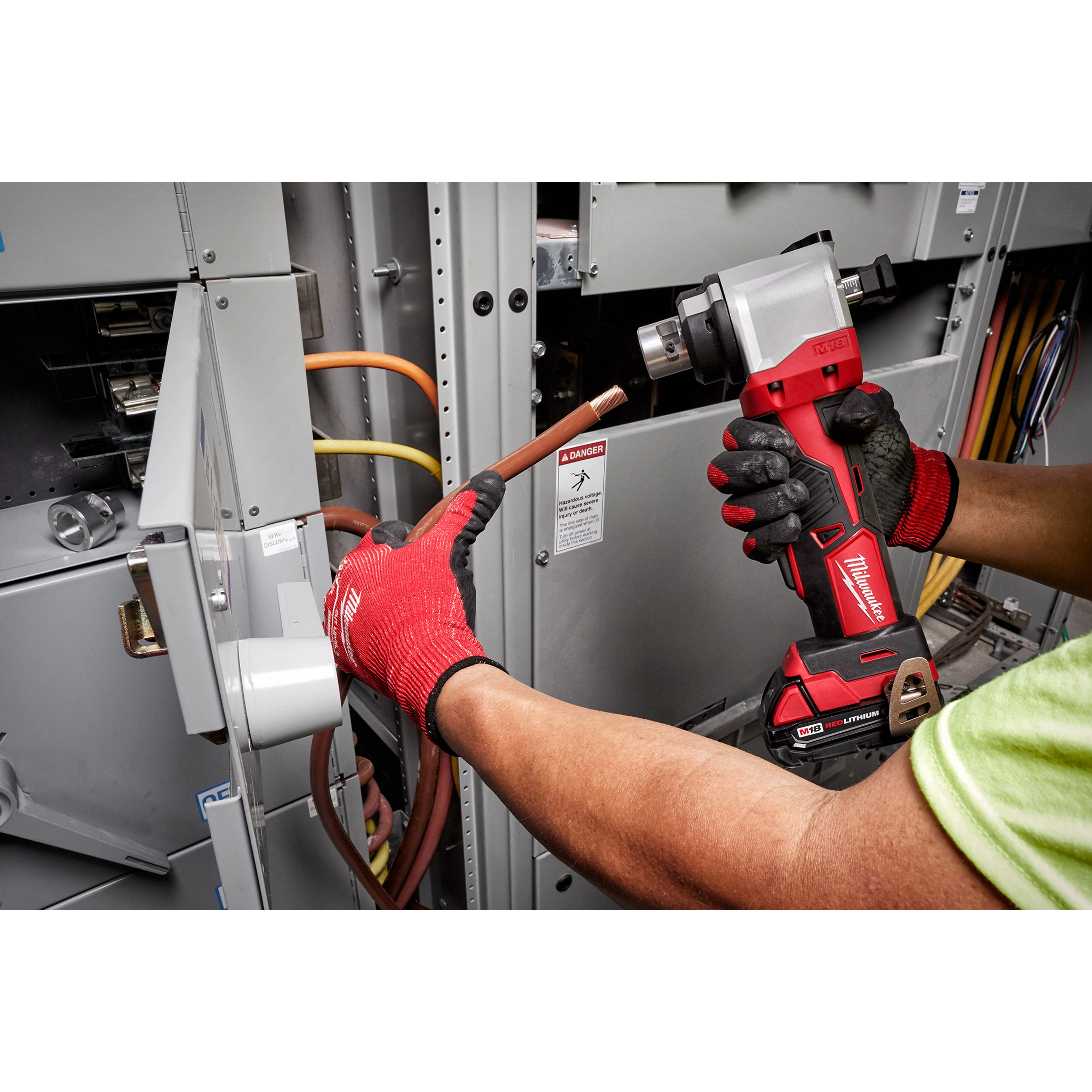 A person uses the M18 Cable Stripper to strip the insulation off electrical wires in an industrial electrical panel.