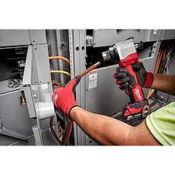 A person uses the M18 Cable Stripper to strip the insulation off electrical wires in an industrial electrical panel.