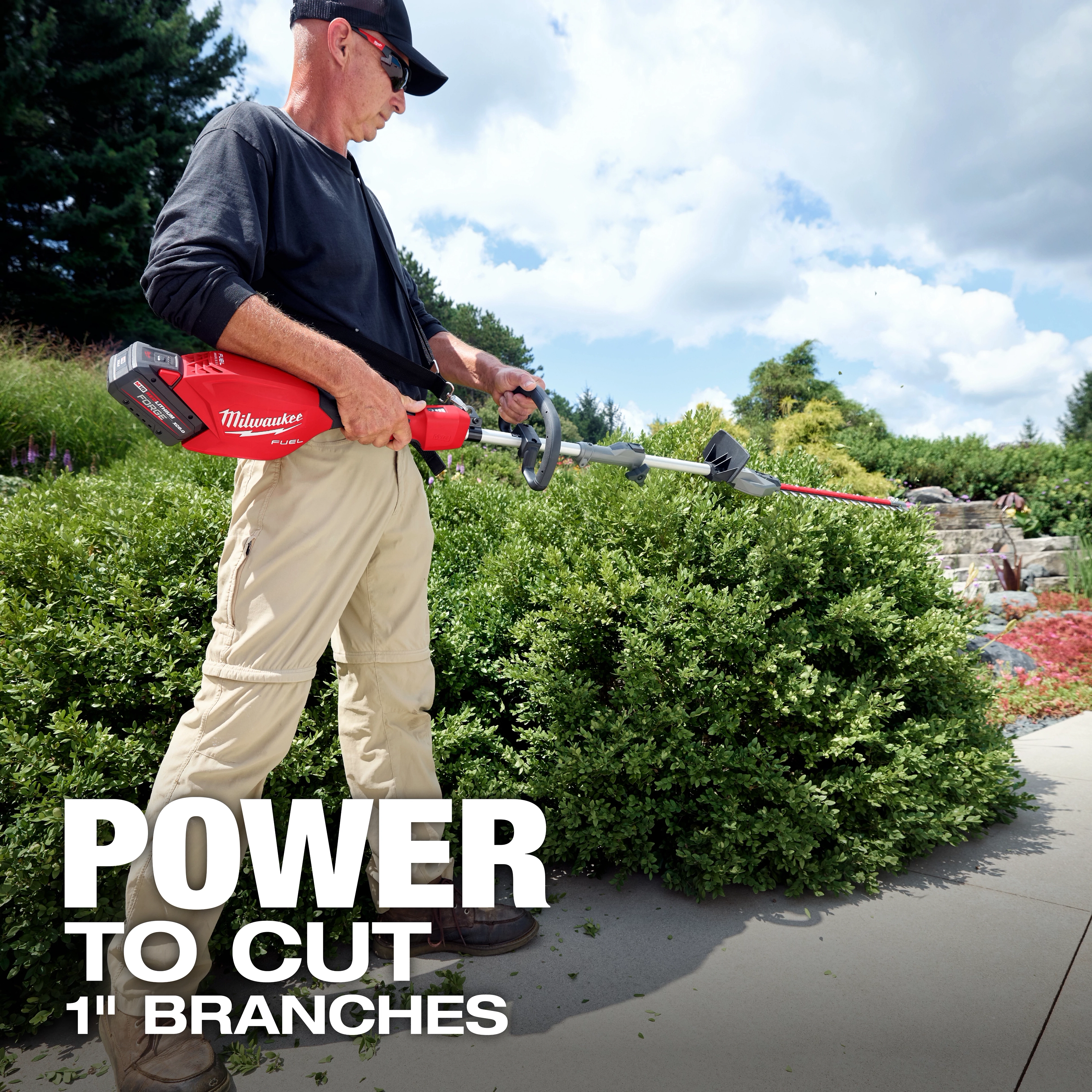 Person trimming a hedge with a QUIK-LOK Short Pole Hedge Trimmer Attachment in a garden walkway.