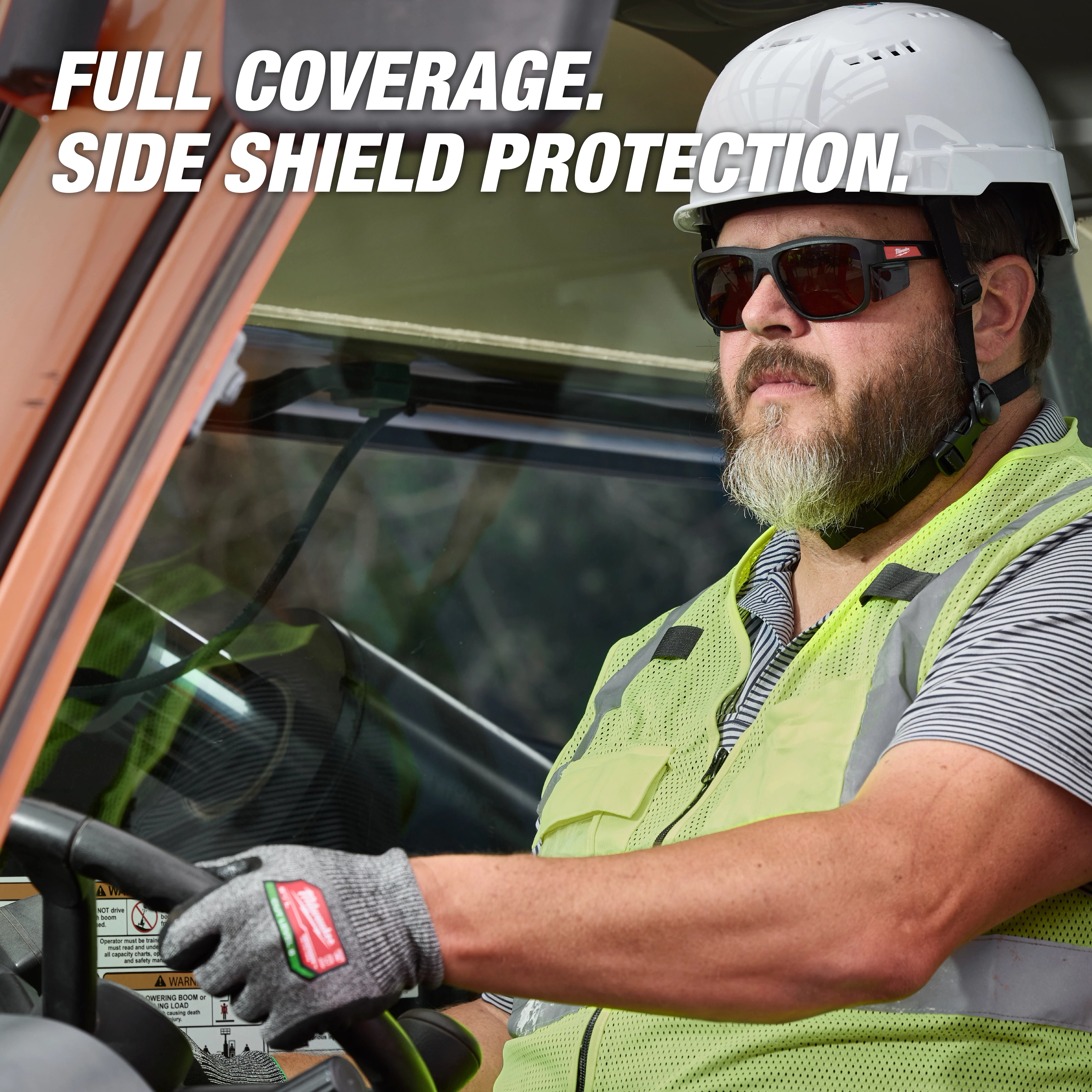 A worker is driving a vehicle, wearing a hard hat, a reflective vest, and Full Frame Safety Glasses with Removable Side Shields – Brown Anti-Scratch Lenses. The text on the image highlights the product's full coverage and side shield protection.