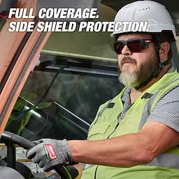 A worker is driving a vehicle, wearing a hard hat, a reflective vest, and Full Frame Safety Glasses with Removable Side Shields – Brown Anti-Scratch Lenses. The text on the image highlights the product's full coverage and side shield protection.