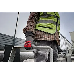 A person wearing an IMPACT CUT 5 NITRILE DIP GLOVE - L, holding a metal bar, dressed in work clothes and a high-visibility vest.