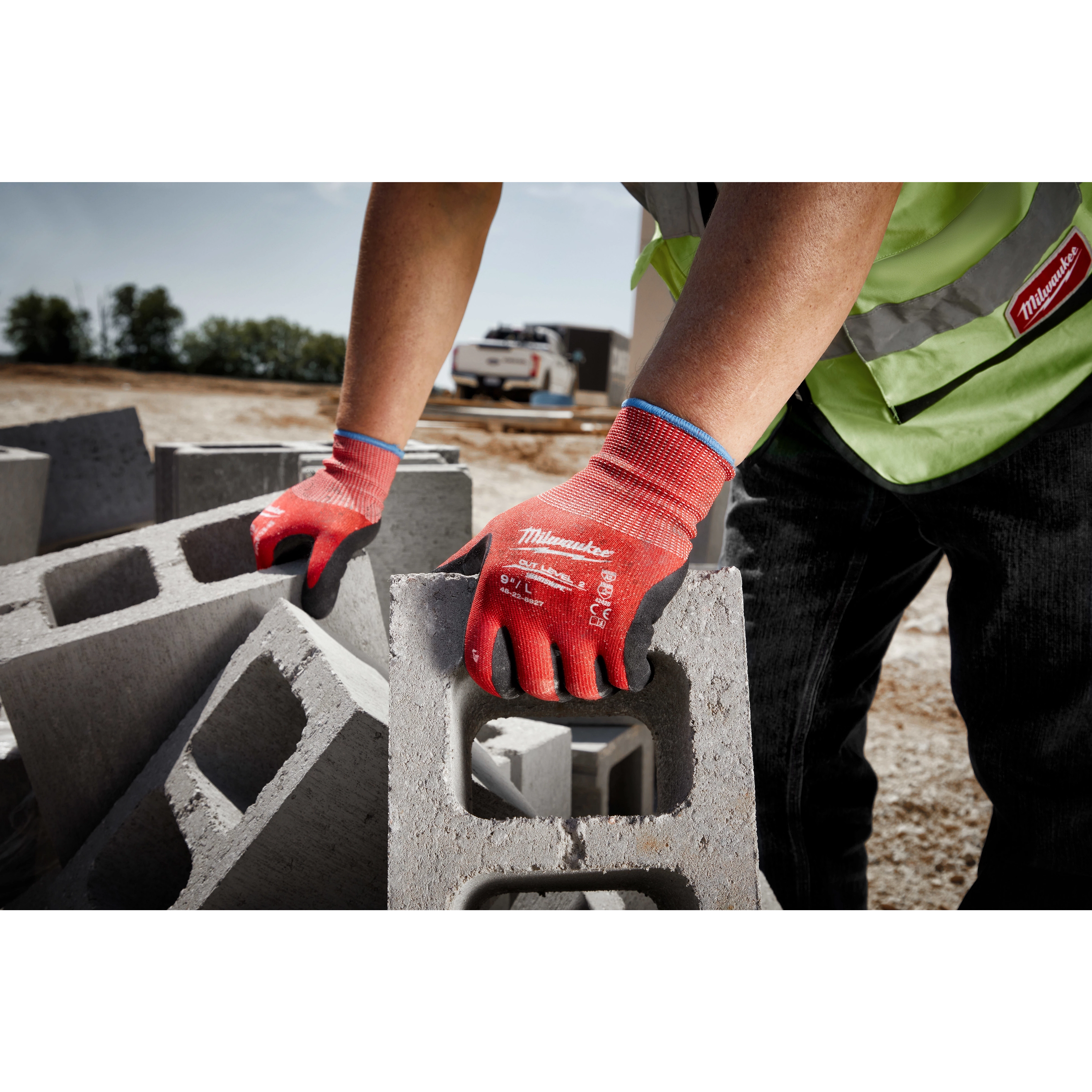 A person wearing Cut Level 2 Nitrile Dipped Gloves - L is lifting a concrete block at an outdoor construction site.
