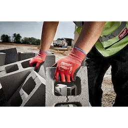 A person wearing Cut Level 2 Nitrile Dipped Gloves - L is lifting a concrete block at an outdoor construction site.
