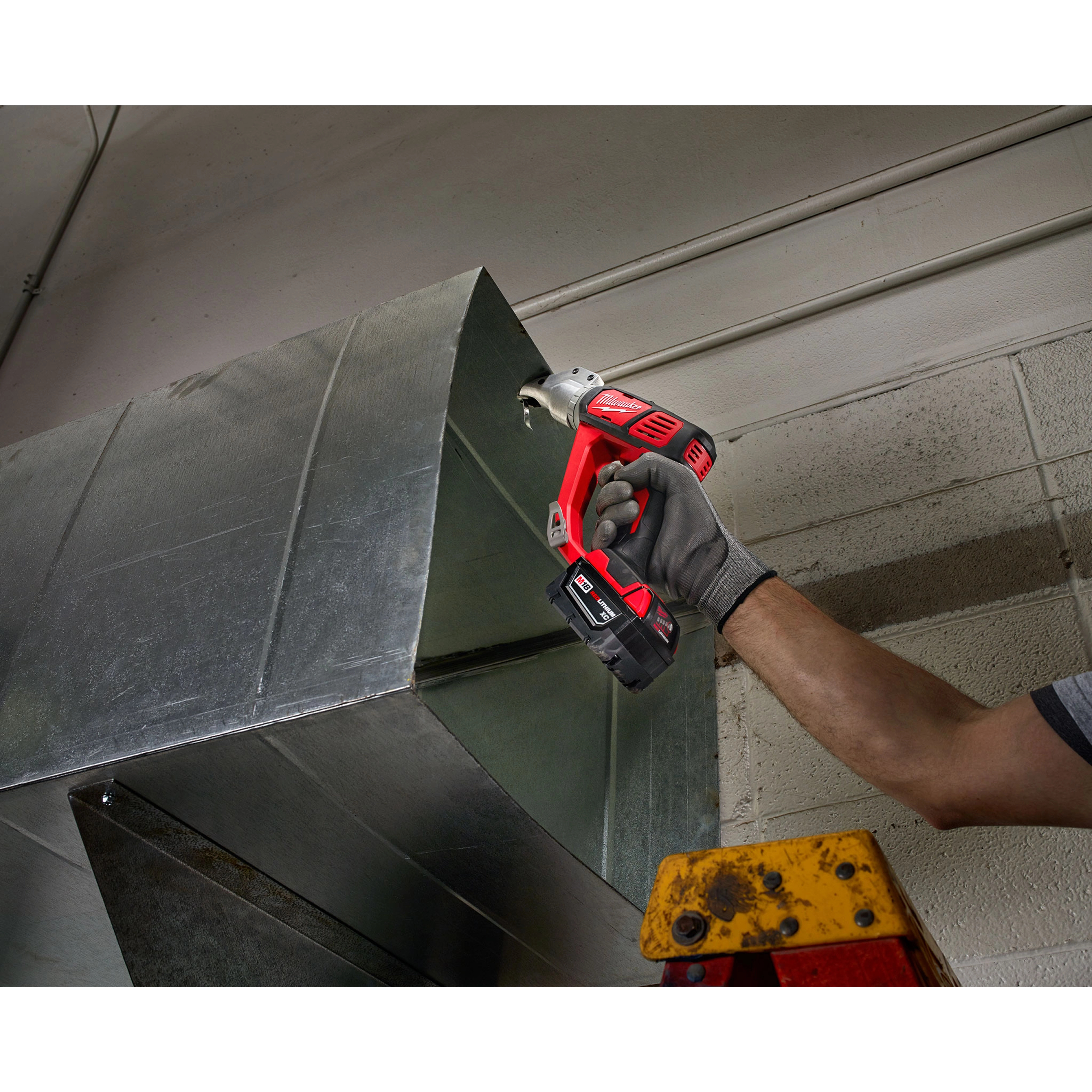 A person using the M18 18 Gauge Double Cut Shear Kit to cut a sheet of metal. The image is taken in an industrial setting.