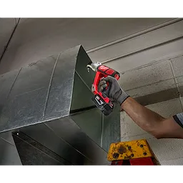 A person using the M18 18 Gauge Double Cut Shear Kit to cut a sheet of metal. The image is taken in an industrial setting.