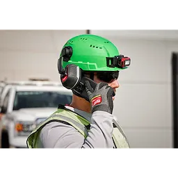 A worker wearing a green hard hat, safety vest, and BOLT 26dB Earmuffs stands in front of a white truck.
