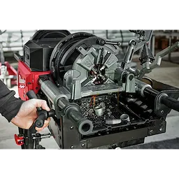 Person operating MX FUEL Pipe Threading Machine with metal pipes and oil shavings visible, showcasing threading process.
