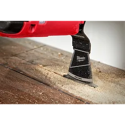 The Milwaukee OPEN-LOK 2-1/2" HCS Japanese Tooth PRO-CURVE Hardwood Multi-Tool Blade cutting through a wooden surface.