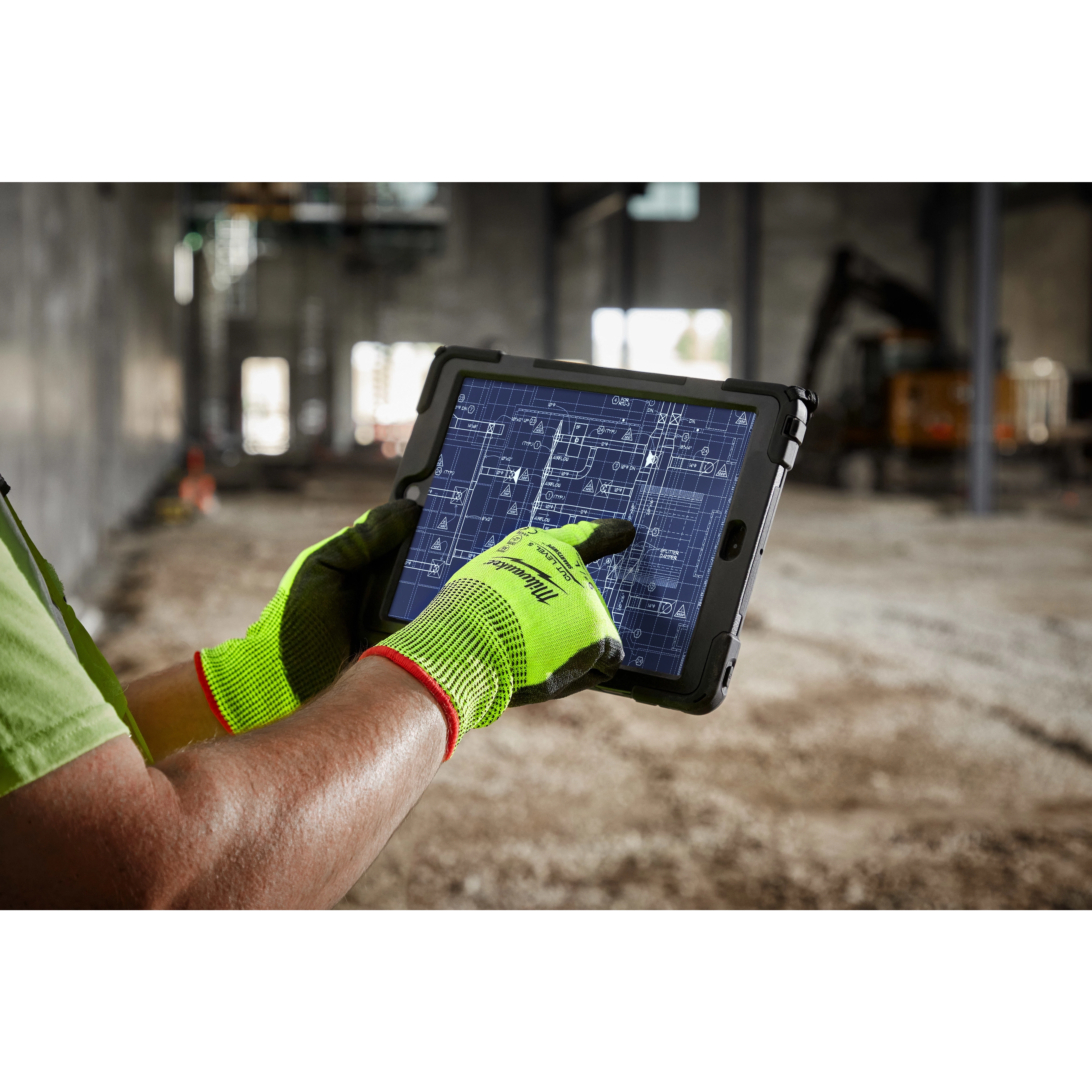 A person wearing high visibility cut level 5 polyurethane dipped gloves - L uses a tablet displaying a blueprint in a construction site.
