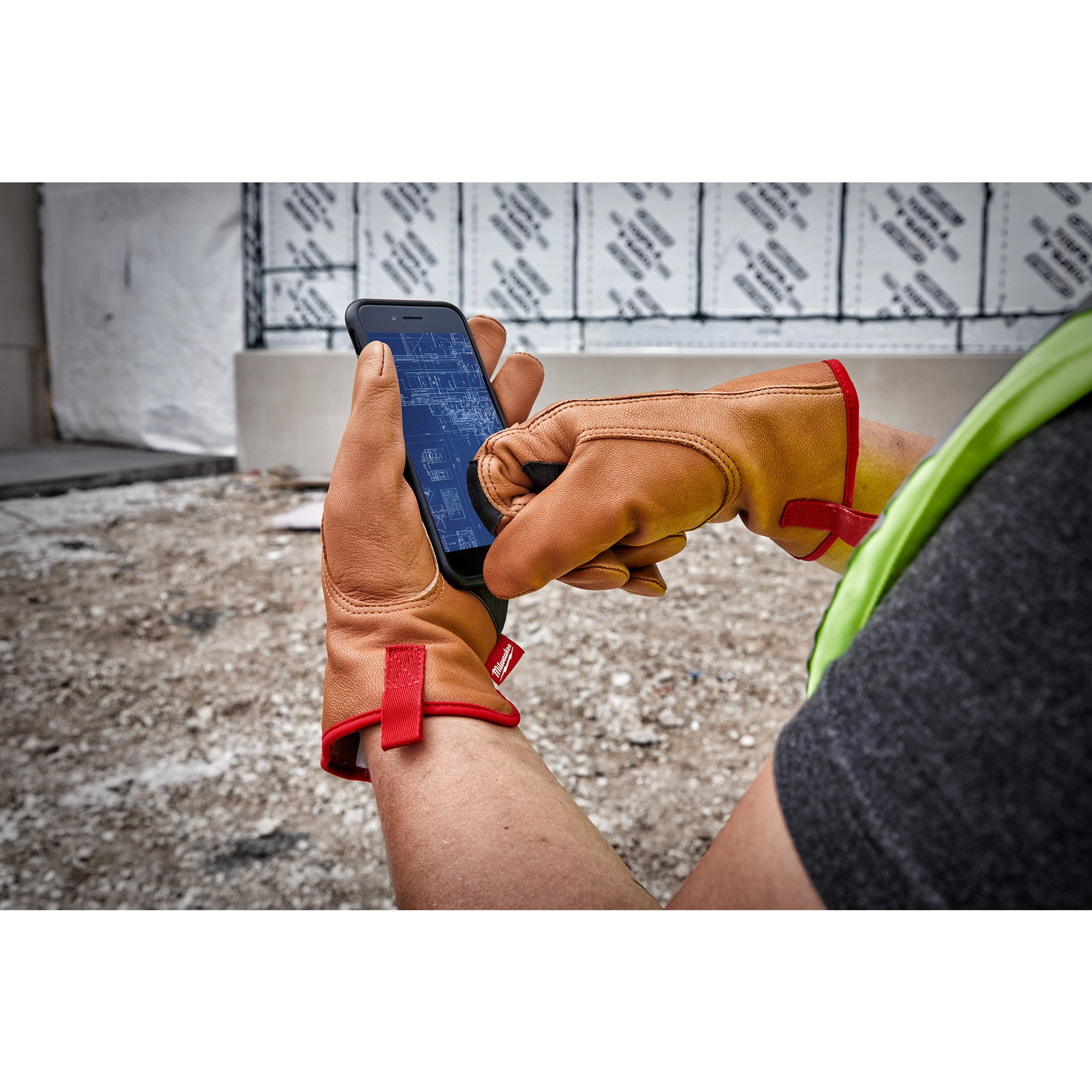 Person wearing Goatskin Leather Gloves uses a smartphone at a construction site, with red fabric accents on the gloves.