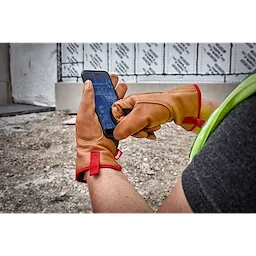Person wearing Goatskin Leather Gloves uses a smartphone at a construction site, with red fabric accents on the gloves.