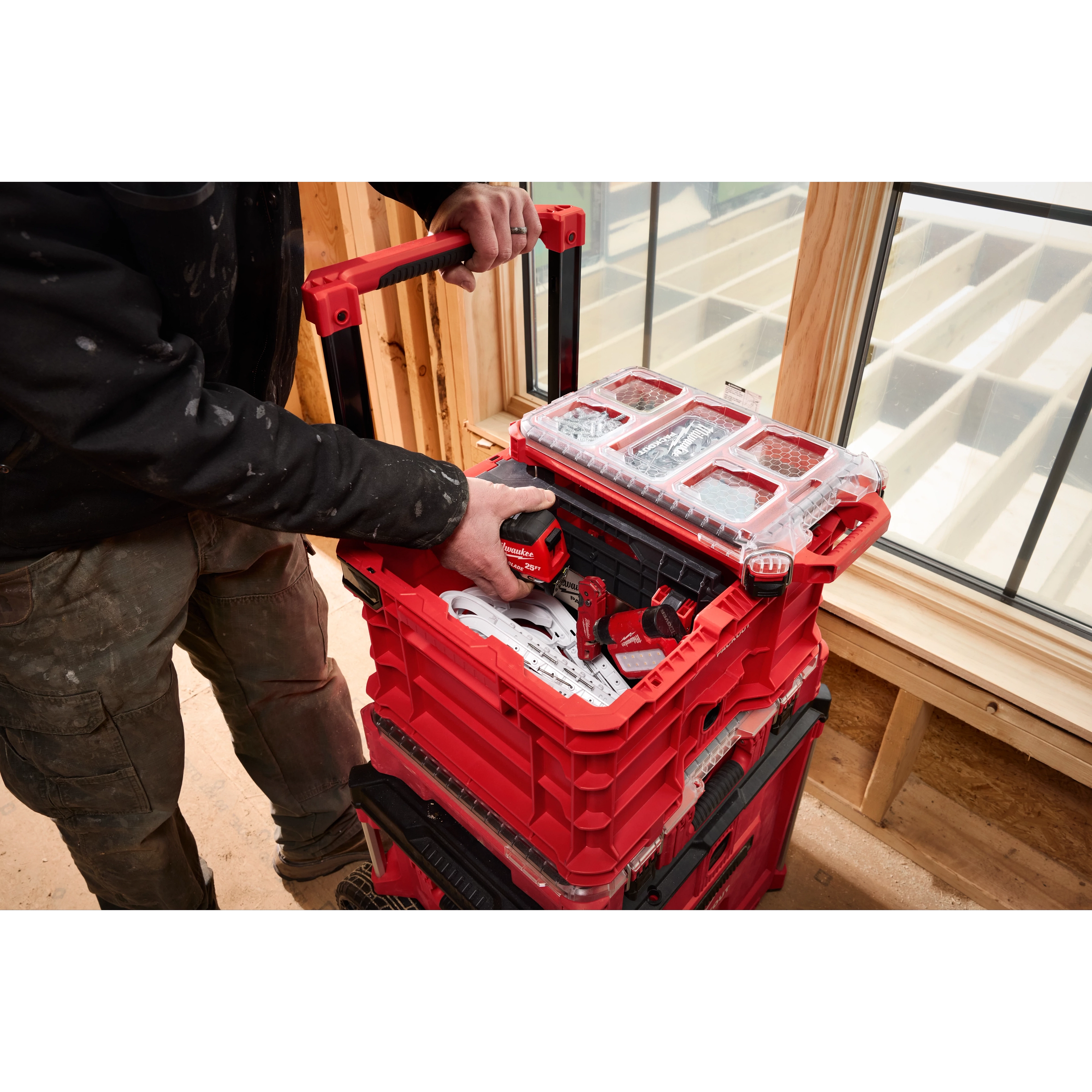 A man using the Divider for PACKOUT Crate to organize red power tools and accessories in a red stacking toolbox on a construction site.