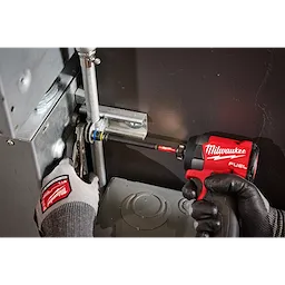 A person is using the SHOCKWAVE™ Impact Duty 5/16” and 3/8” x 6” QUIK-CLEAR™ 2-in-1 Magnetic Nut Driver attached to a red Milwaukee Fuel power tool to tighten a pipe fitting. The individual is wearing Milwaukee-branded work gloves. The setting is an industrial environment.