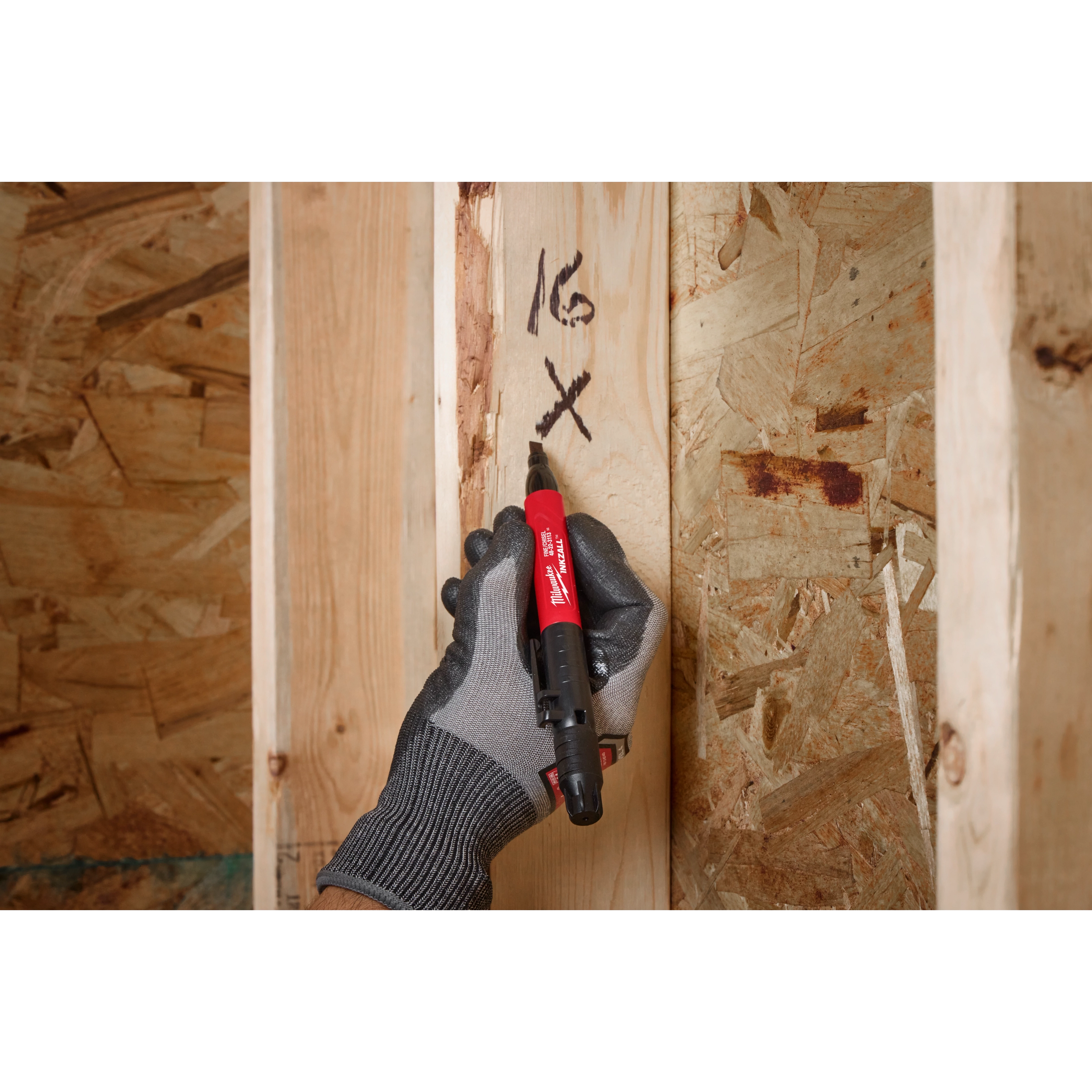 A gloved hand using the INKZALL Double-Sided Black Jobsite Marker. Fine Point & Chisel Tip to write markings on a wooden beam. The pen is used in construction settings for precise marking.