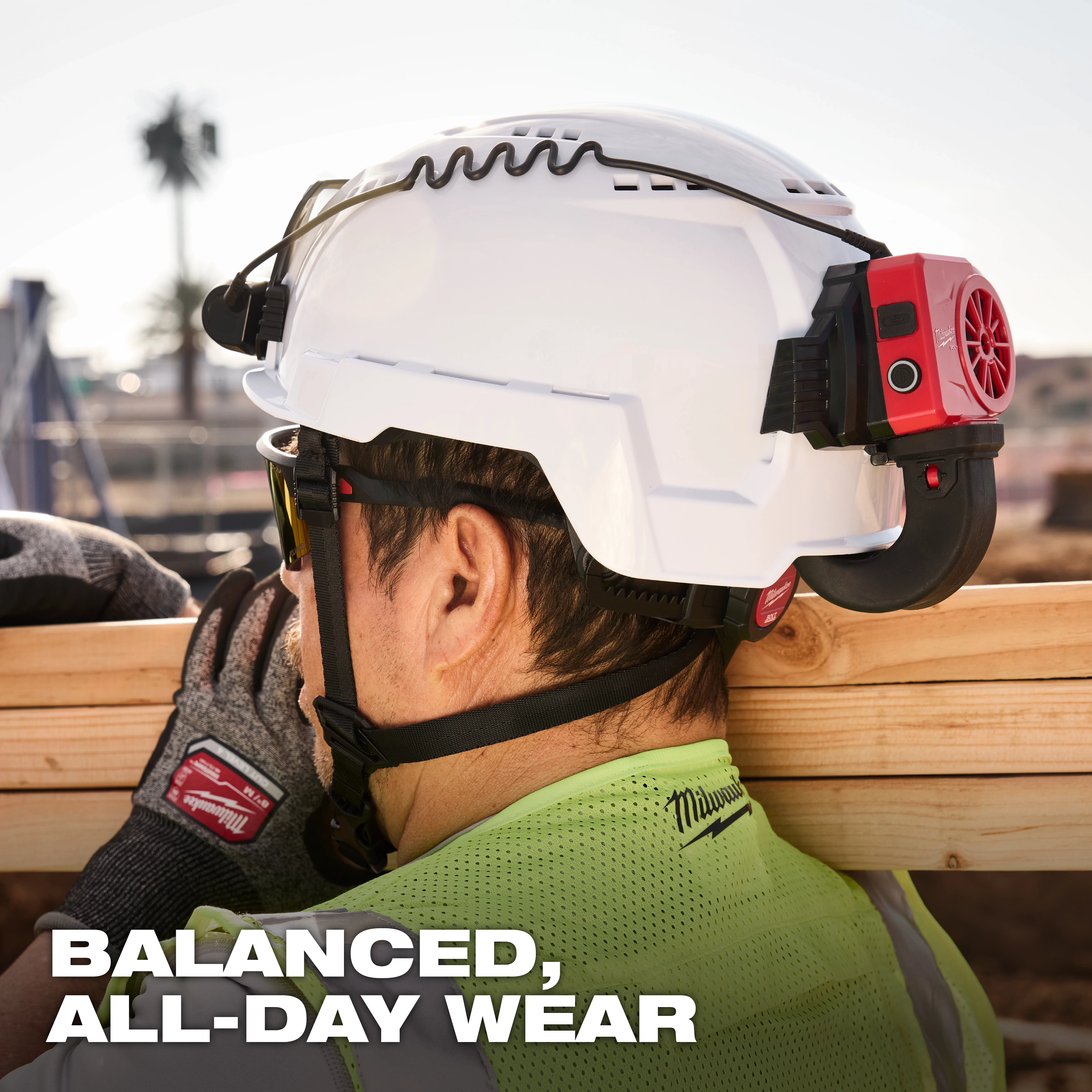 Worker wearing a white helmet equipped with BOLT REDLITHIUM USB Cooling Fan, lifting a wooden beam. Text: "Balanced, All-Day Wear".
