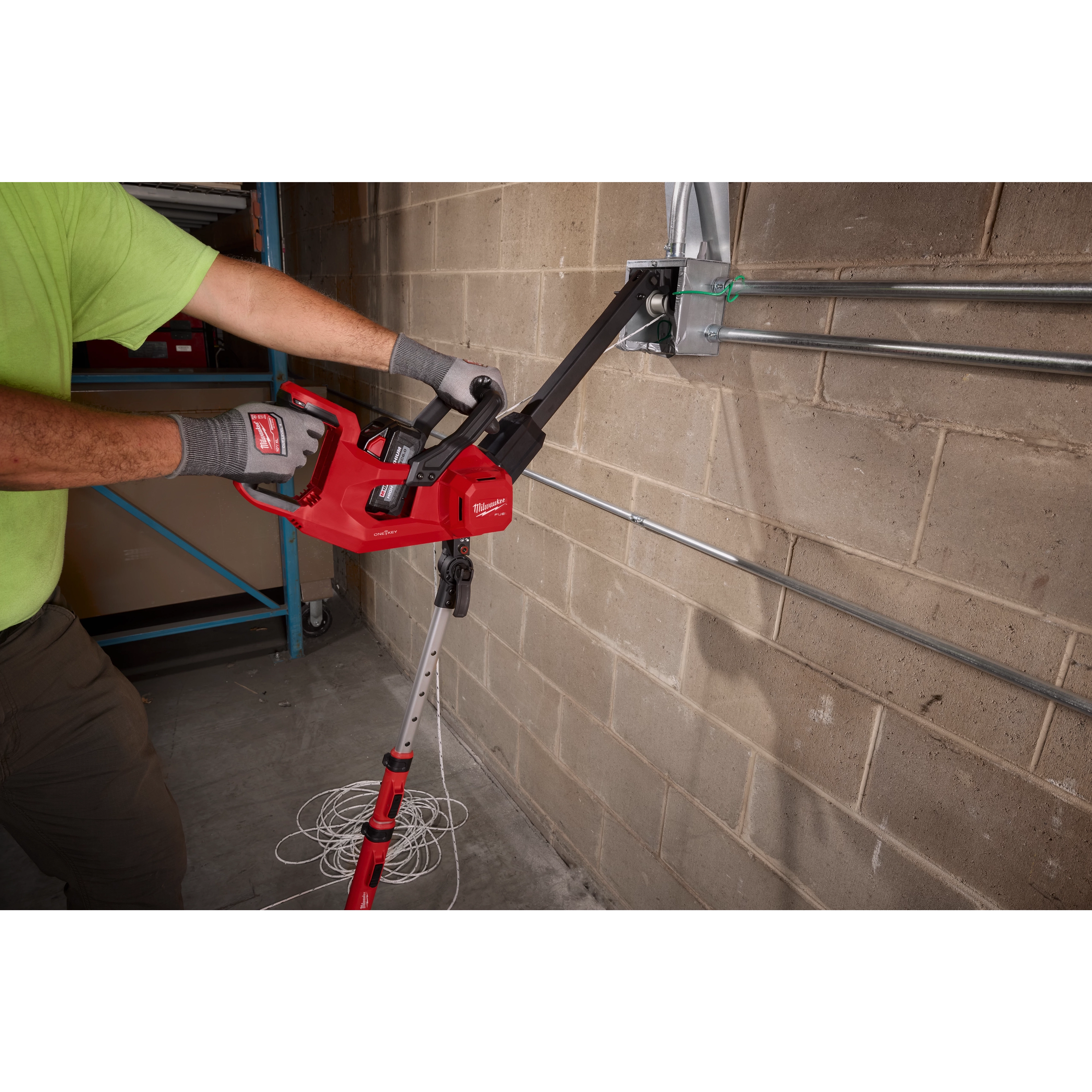 Worker using an M18 FUEL 1K Wire Puller to pull wire through conduits on a concrete block wall.