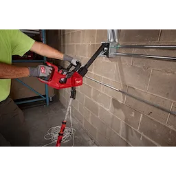 Worker using an M18 FUEL 1K Wire Puller to pull wire through conduits on a concrete block wall.