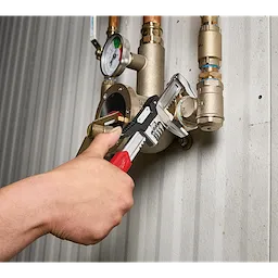 12” Quick Adjust Smooth Jaw Wrench gripping a pipe fitting on a wall-mounted valve and gauge assembly.