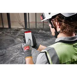 Worker wearing Cut Level 8 High-Dexterity Nitrile Dipped Gloves - L operates a smartphone in a construction setting.