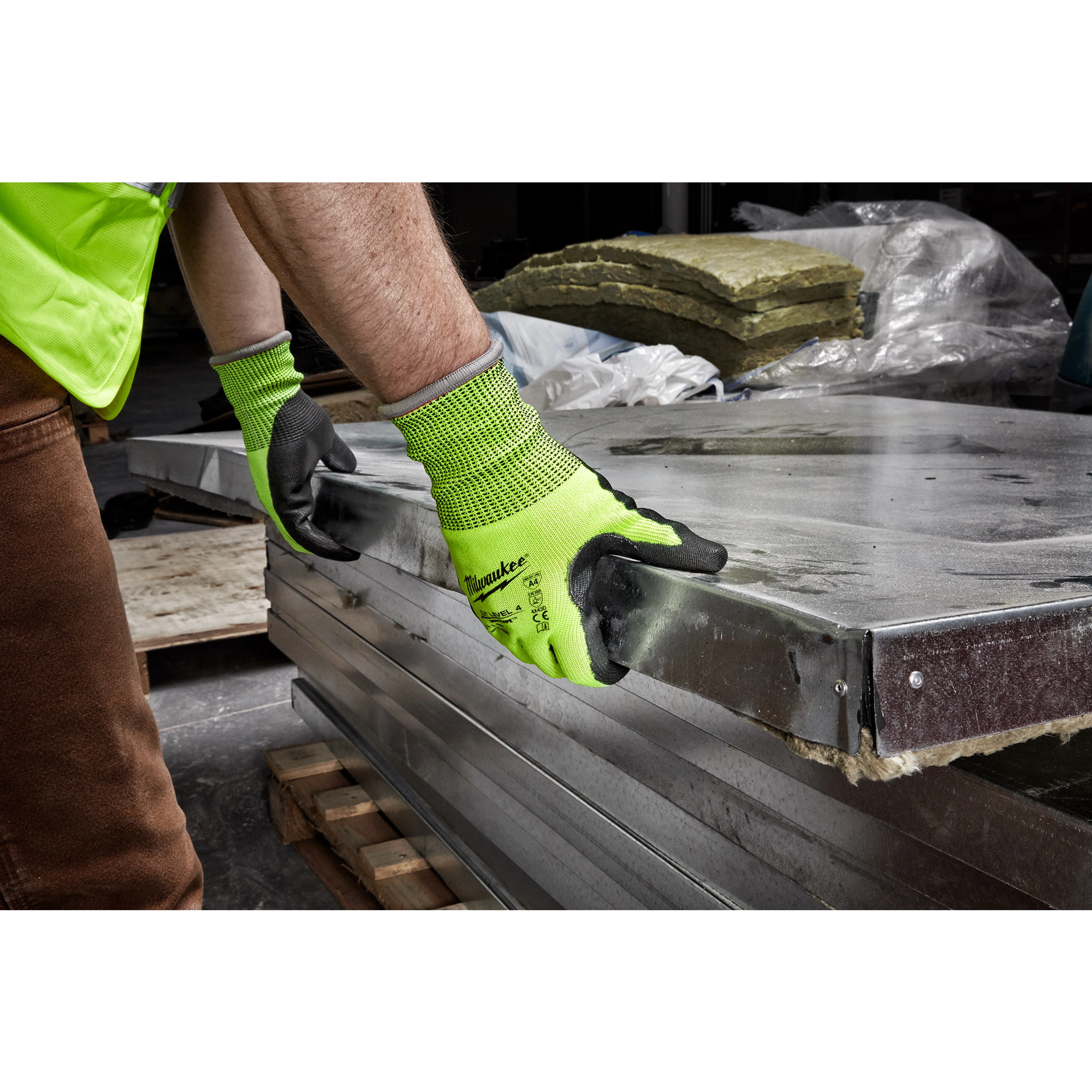 Person wearing Hi Vis Cut Gloves handling large metal sheets in a construction or warehouse setting.