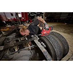 Worker using an M18 FUEL Grease Gun on a truck’s rear wheel assembly in a garage.