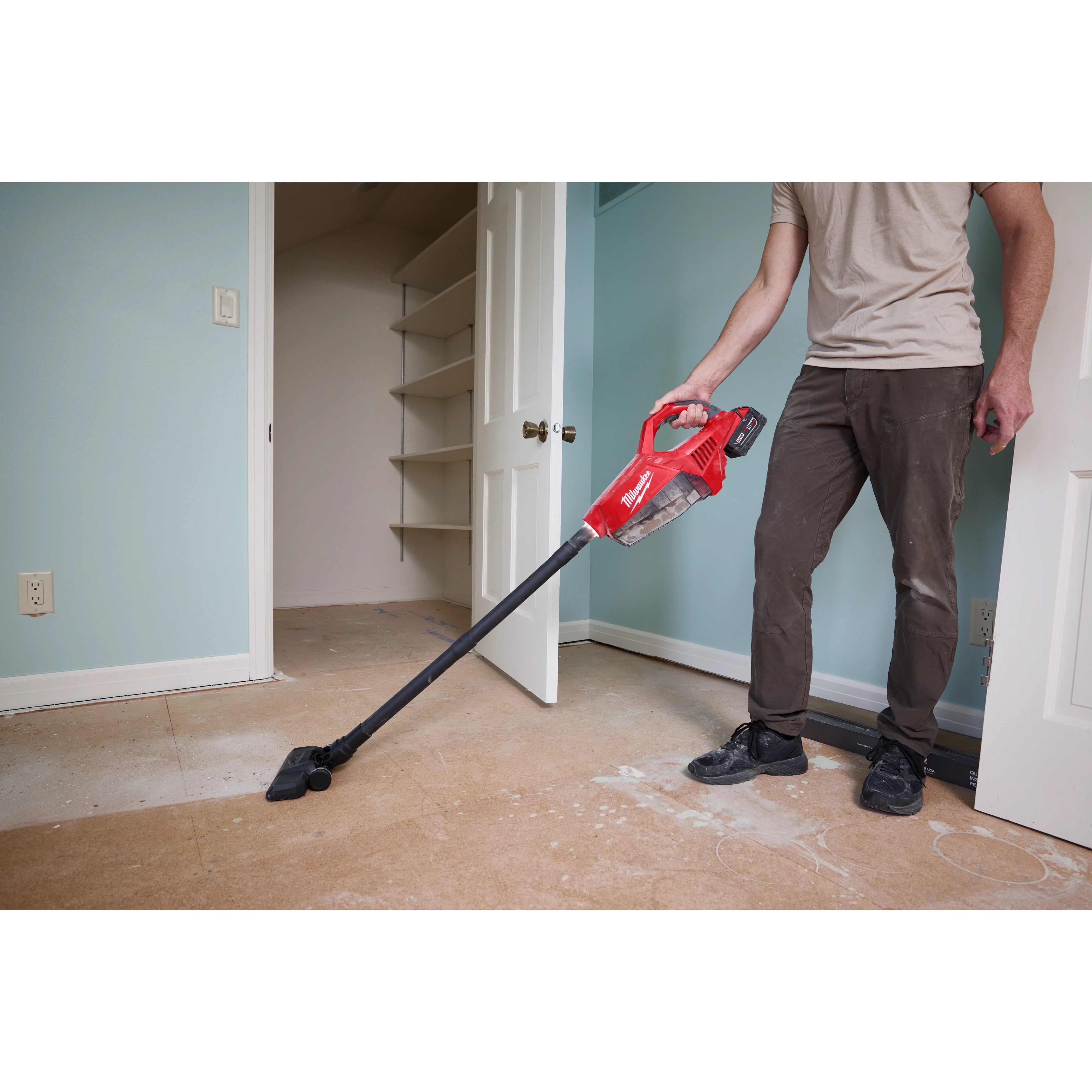 A person vacuums a dusty floor using an M18 Brushless Handheld Vacuum in a partially renovated room.