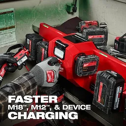 The M18™ and M12™ Gangbox Rapid Charger is displayed charging multiple battery packs in a workshop setting. A person wearing gloves is holding a Milwaukee battery pack near the charger. Text on the image highlights faster charging for M18™, M12™, and devices.