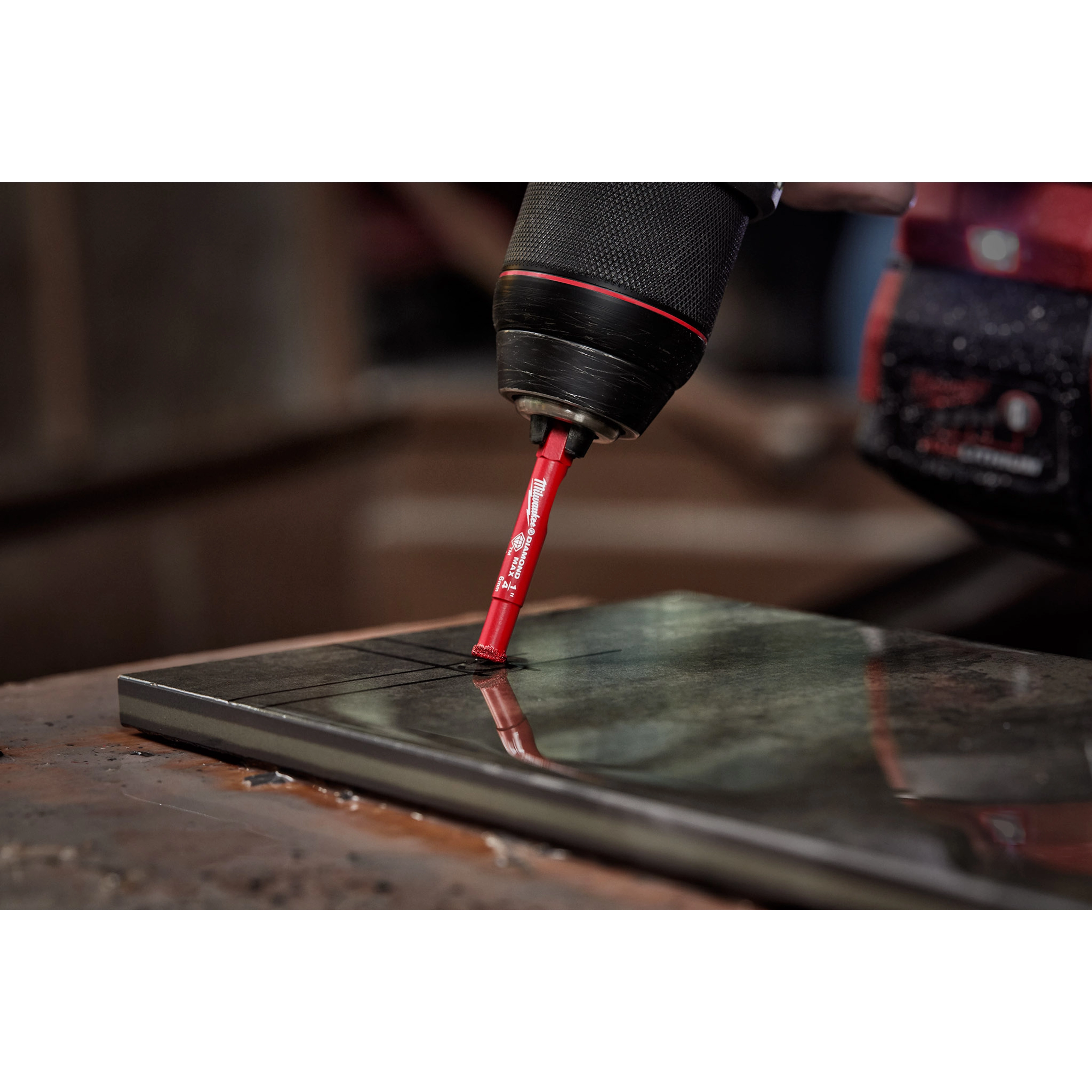A close-up of a power drill using a 1/4" Diamond Grit Hole Saw to drill precise holes in a black tile.
