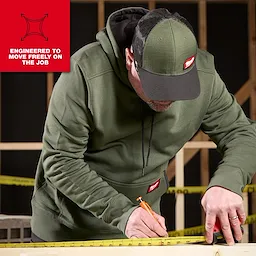 Person wearing a FREEFLEX Pullover Hoodie measuring wood with a tape measure and pencil on a workbench.