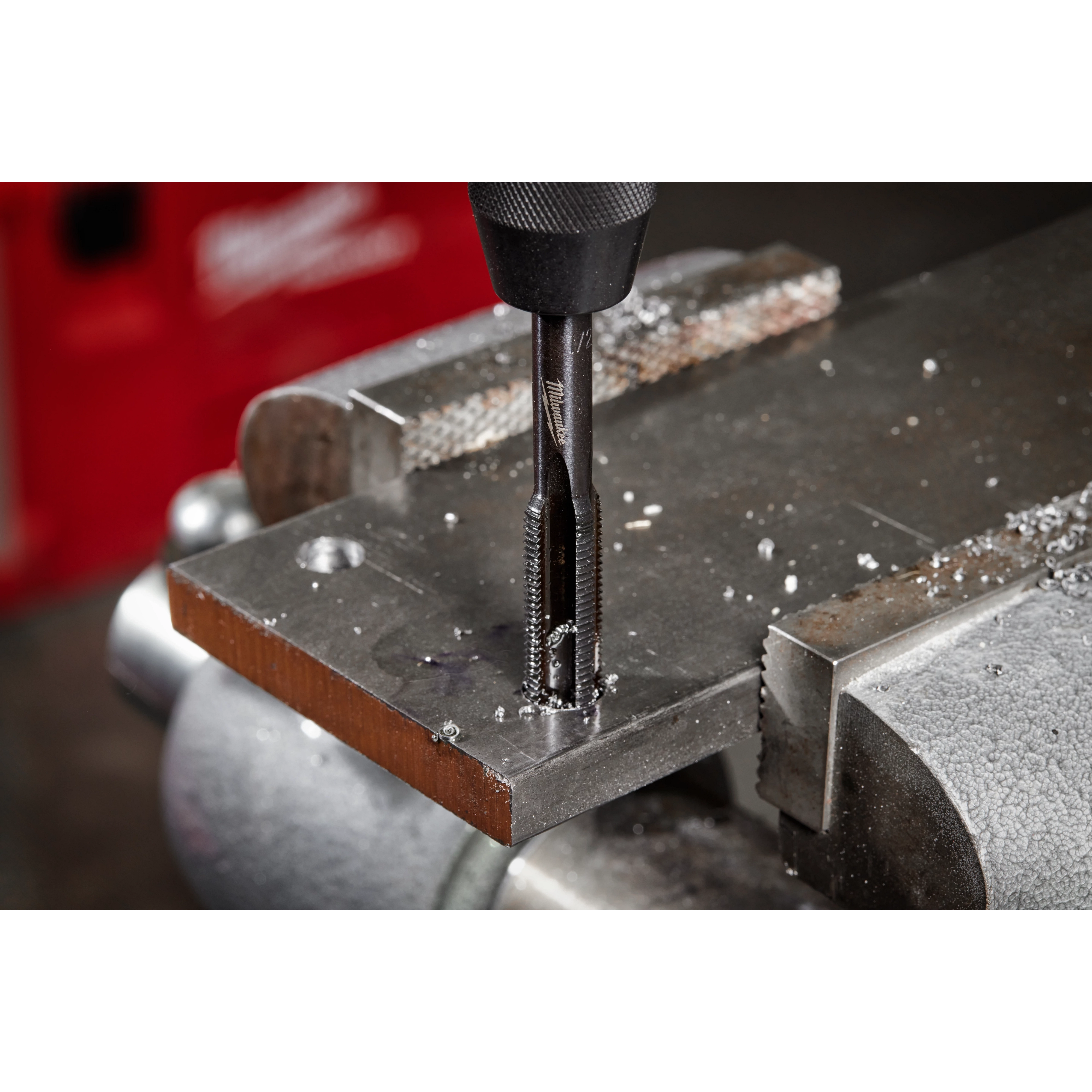 The 1/2"-13 NC Straight Flute Plug Tap is shown in use, mounted on a drill press and creating threads in a metal plate clamped in a vise. Metal shavings are visible around the freshly tapped hole.