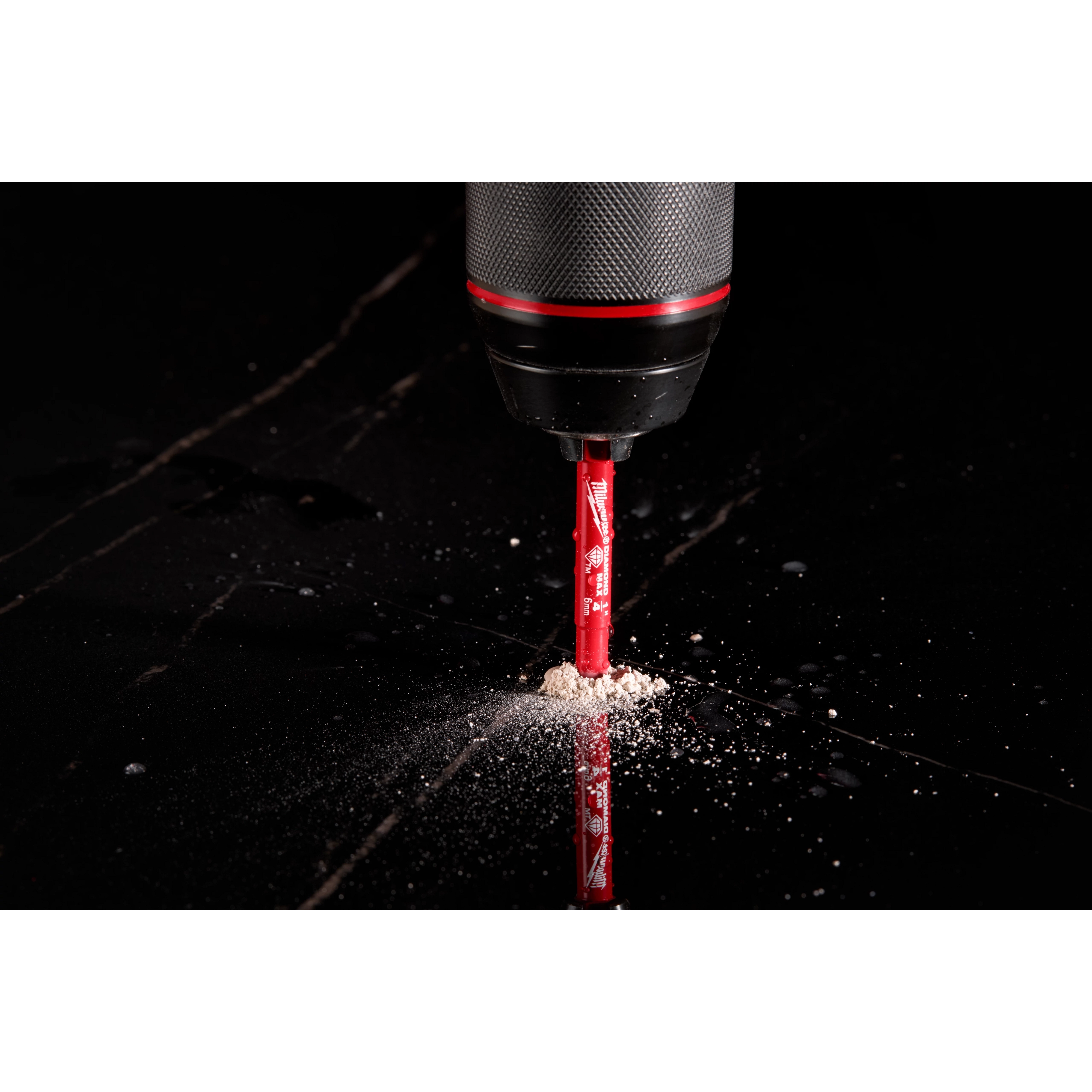 A close-up of a Milwaukee® 1/4" DIAMOND MAX™ Hole Saw Bit being used with a drill on a black surface, producing dust as it drills.