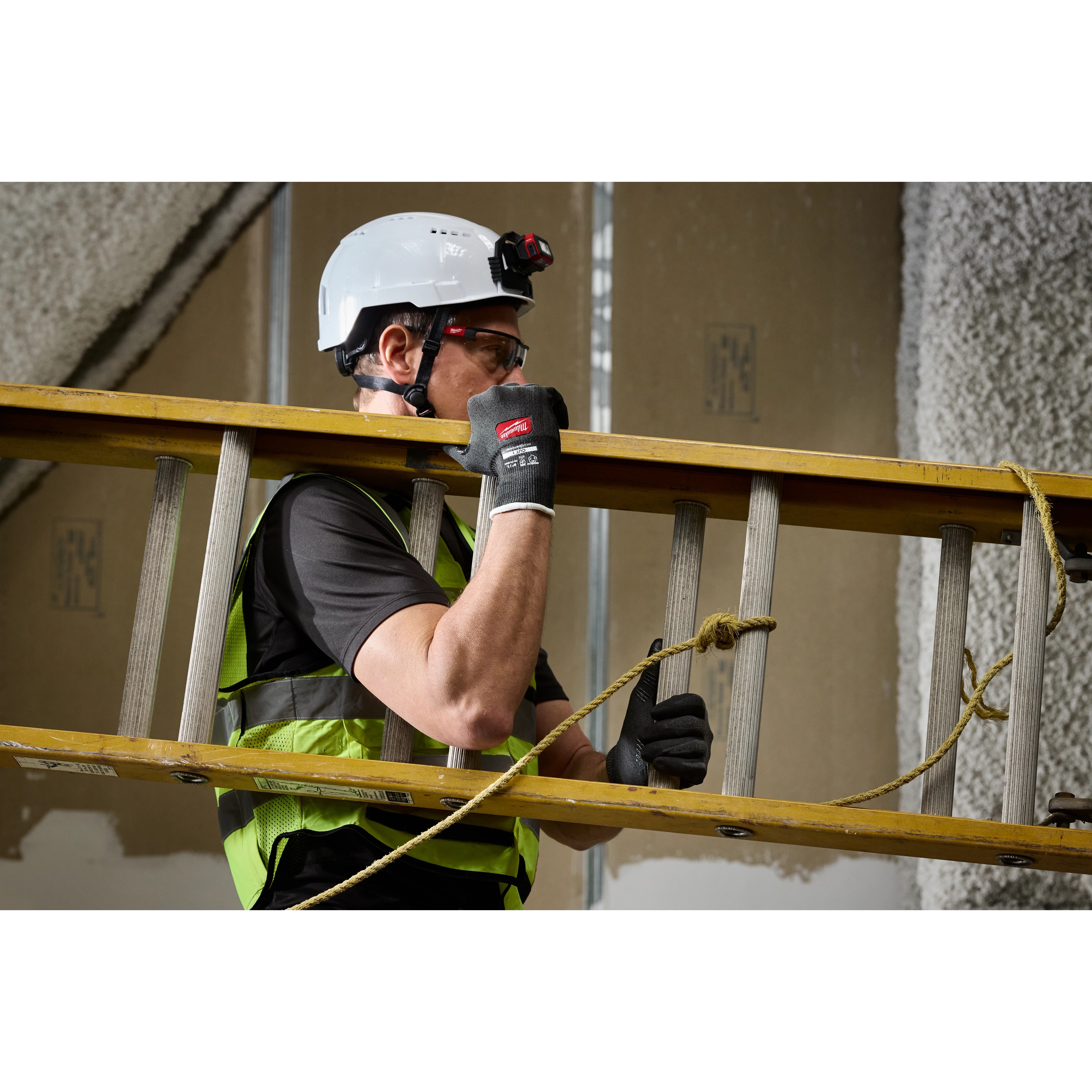 Worker carrying a ladder indoors wearing Cut Level 1 Nitrile Dipped Gloves w/ WEAR-DEFENSE Protection.