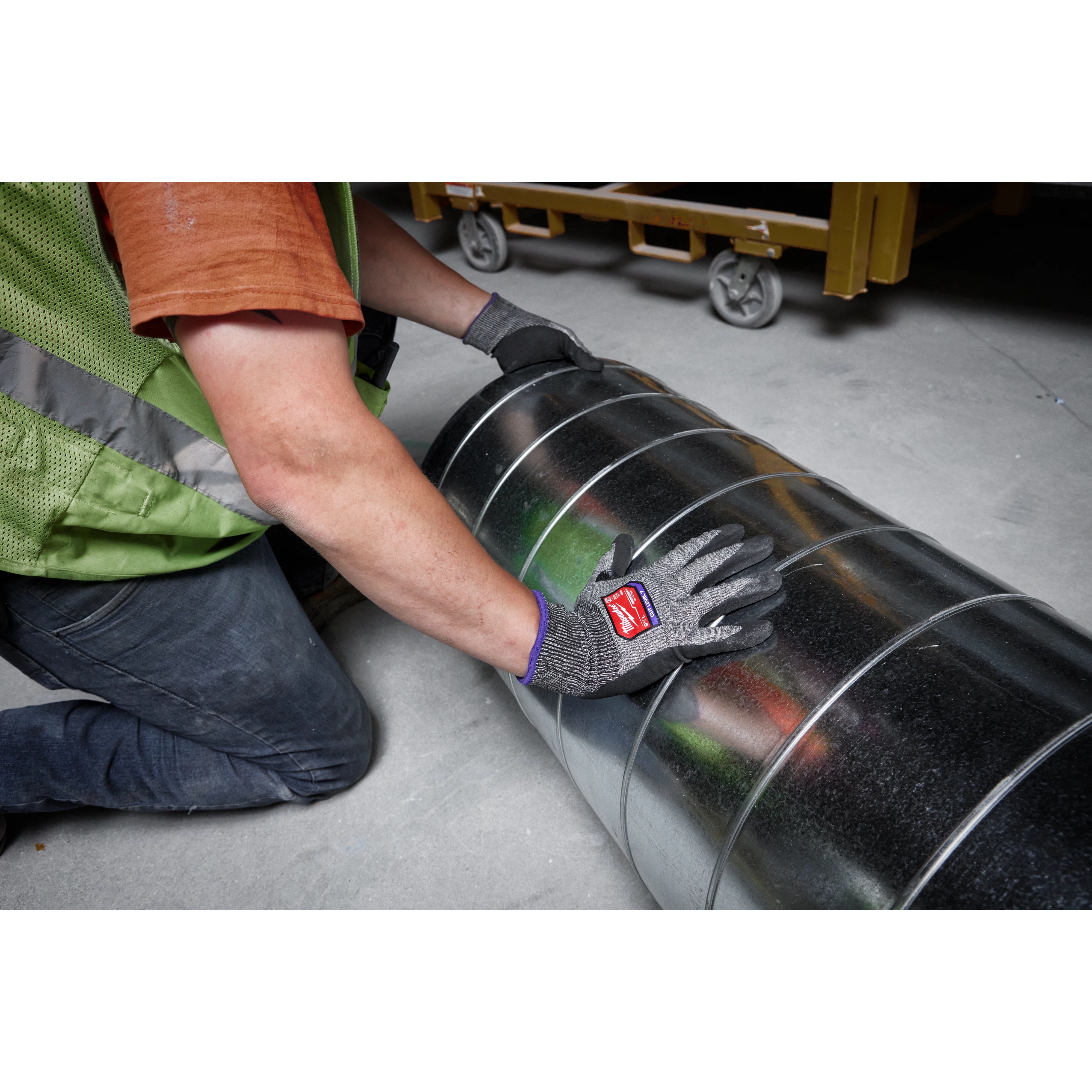 Person wearing Cut Level 7 High-Dexterity Nitrile Dipped Gloves - L, handling a large metallic duct in a construction site.